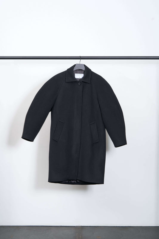COCOON COAT hanging on display showcasing its heavyweight brushed wool fabric and rounded silhouette.