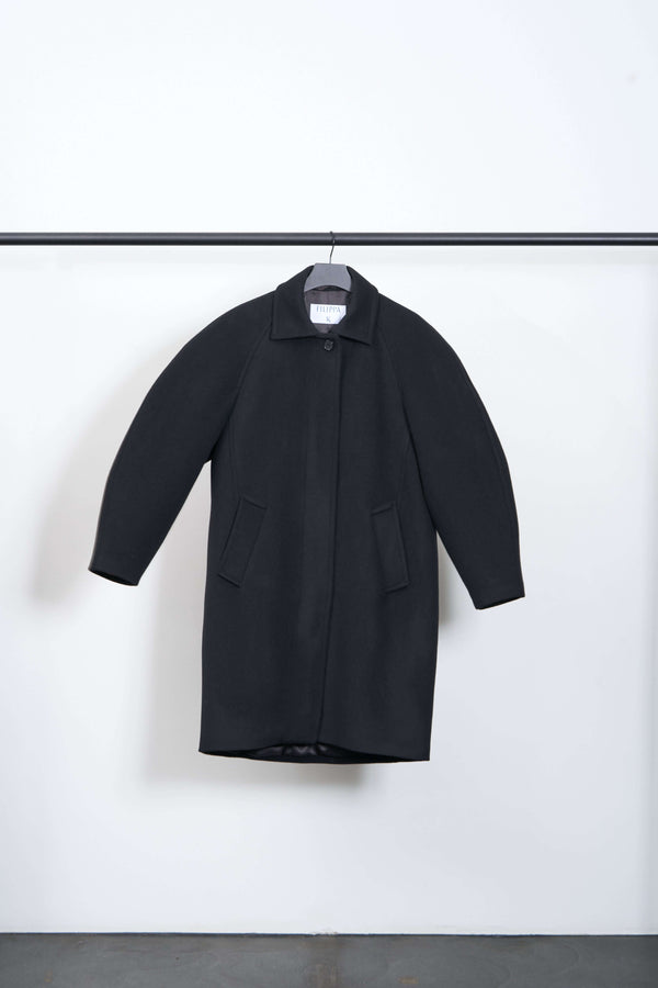 COCOON COAT hanging on display showcasing its heavyweight brushed wool fabric and rounded silhouette.