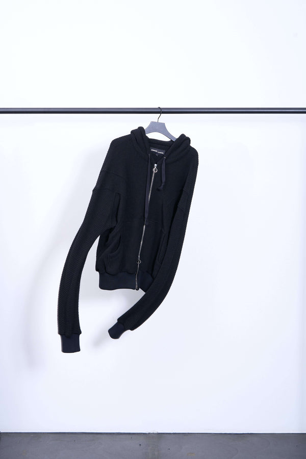 WOOLY ARM FLEX HOODIE displayed on a hanger against a minimalist background, showcasing its unique design and craftsmanship.