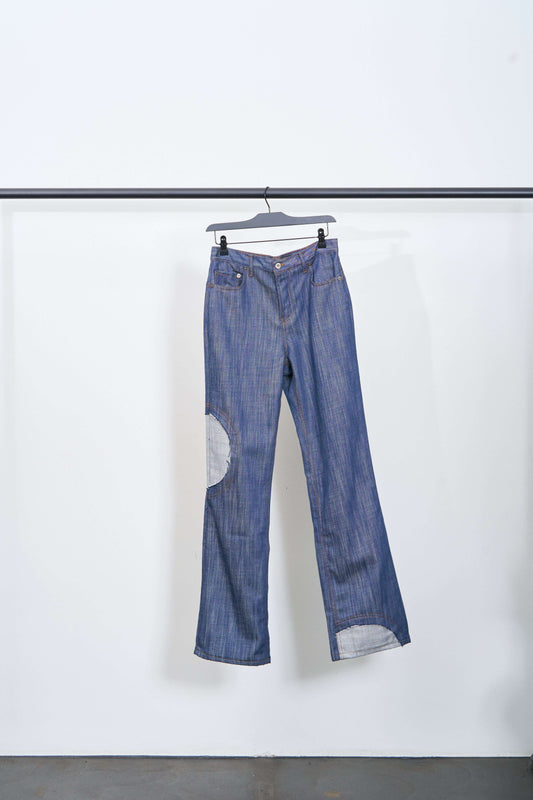 CIRCLE WINDOW JEANS displayed on a hanger, featuring circle cutouts and contrast stitching, made of lightweight raw denim.