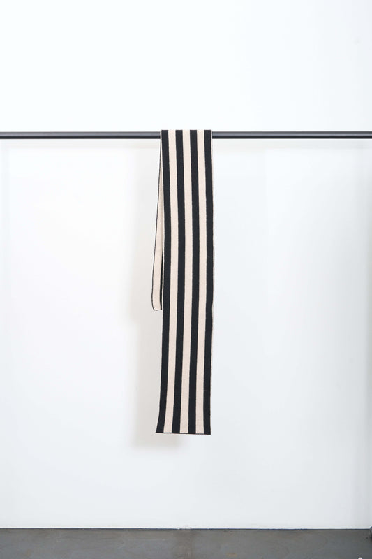 BRUSHED STRIPE SCARF hanging on display, featuring bold contrasting color stripes in black and cream.
