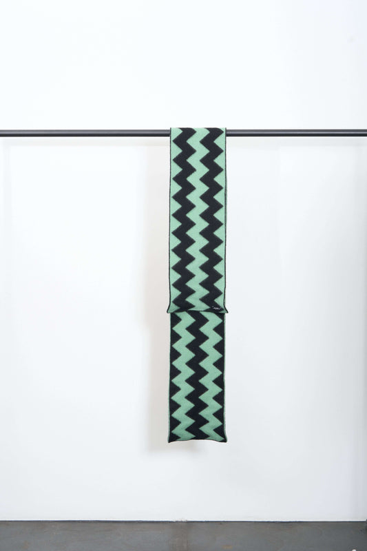 BRUSHED ZIGZAG SCARF hanging on a display rack with a mint green and black zigzag pattern.