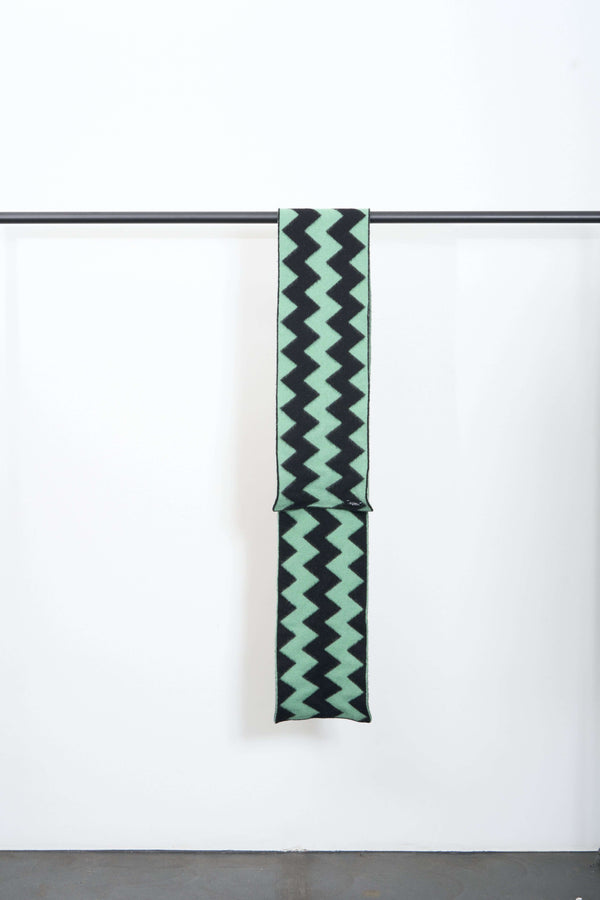 BRUSHED ZIGZAG SCARF hanging on a display rack with a mint green and black zigzag pattern.