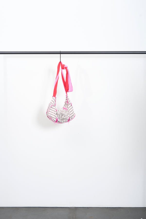 CREMĀ BAG hanging on a clothing rack, made of 100% cotton with a vibrant pink strap.
