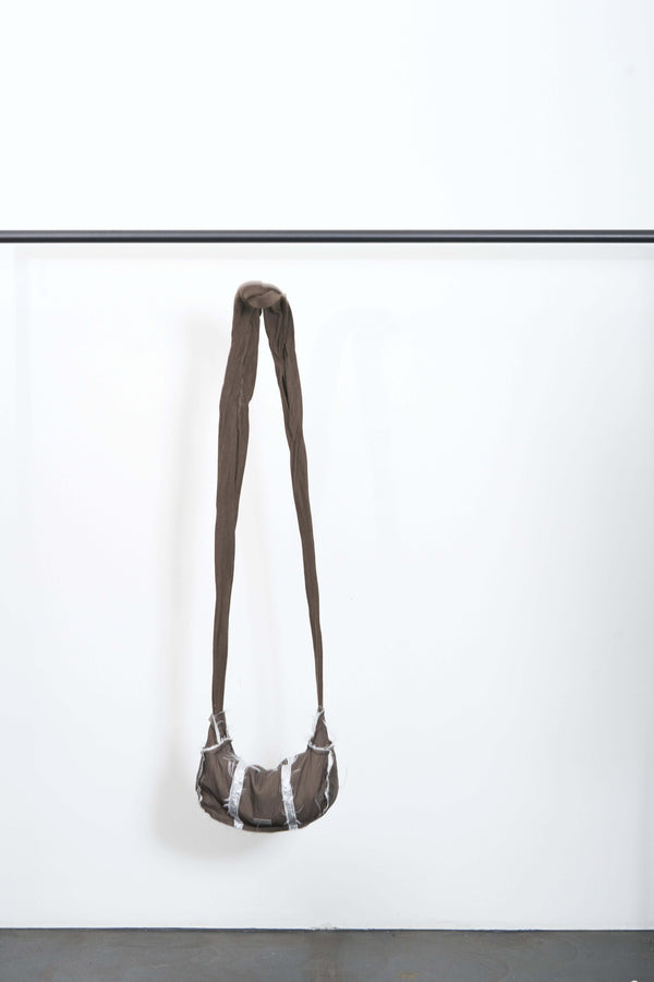 FALLAS BAG with fringed contrasting details, zip closure, and super long strap hanging on a white wall.