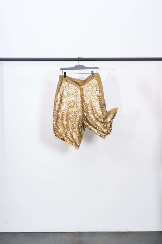 HAND EMBROIDERED TAILORED SHORT hanging display with shimmering golden sequins in bright light.