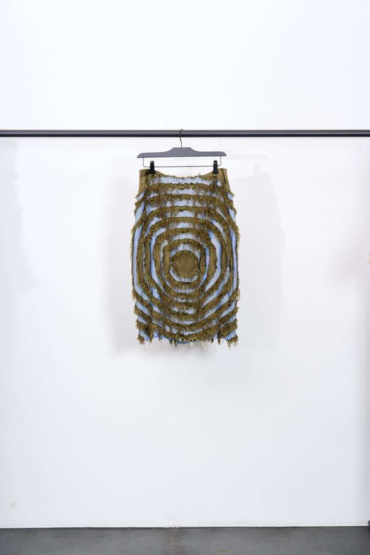 ENCOMPASSING VORTEX SKIRT hanging on a rack showcasing its frayed vortex pattern in khaki and two-tone blue.