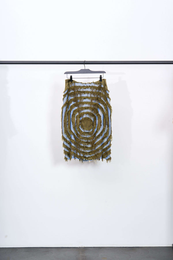 ENCOMPASSING VORTEX SKIRT hanging on a rack showcasing its frayed vortex pattern in khaki and two-tone blue.