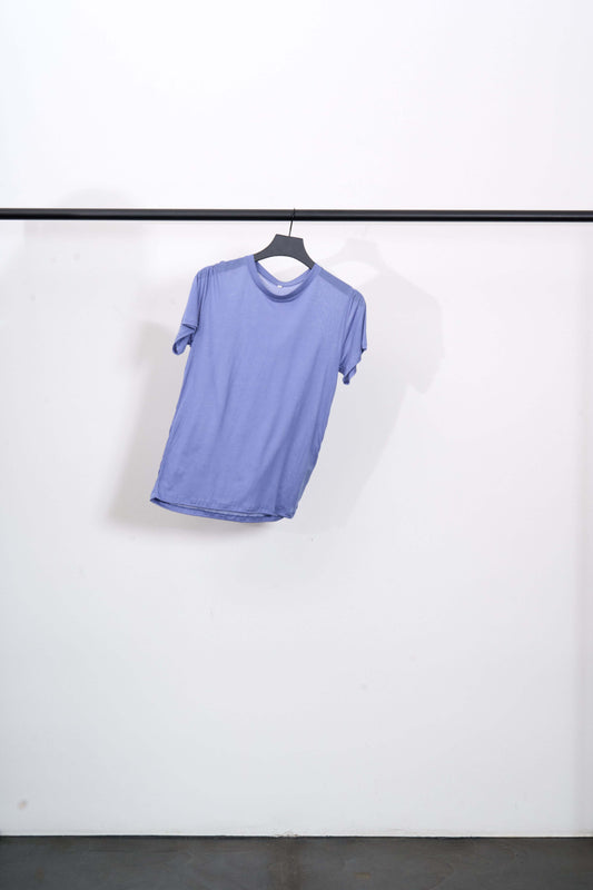 TEE SHIRT in light purple color hanging on a black clothing rack against a white wall.