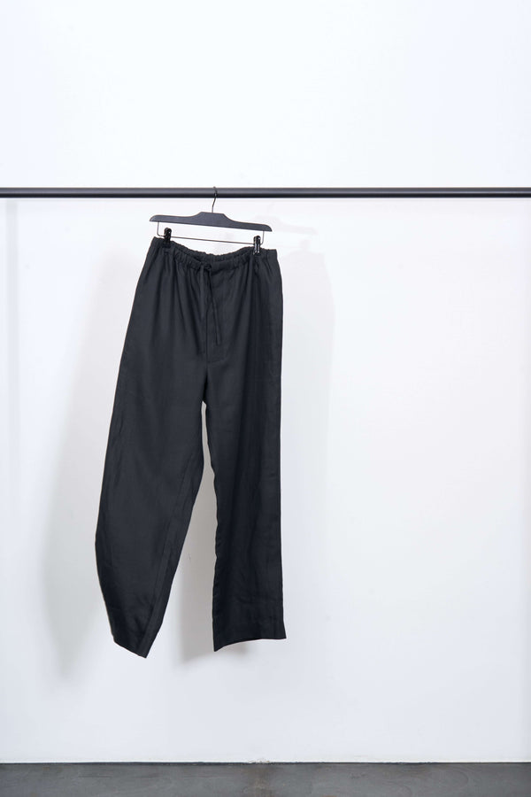 LINEN DRAWSTRING TROUSERS hanging on a rack, made of 100% linen in black color, featuring a straight leg design.