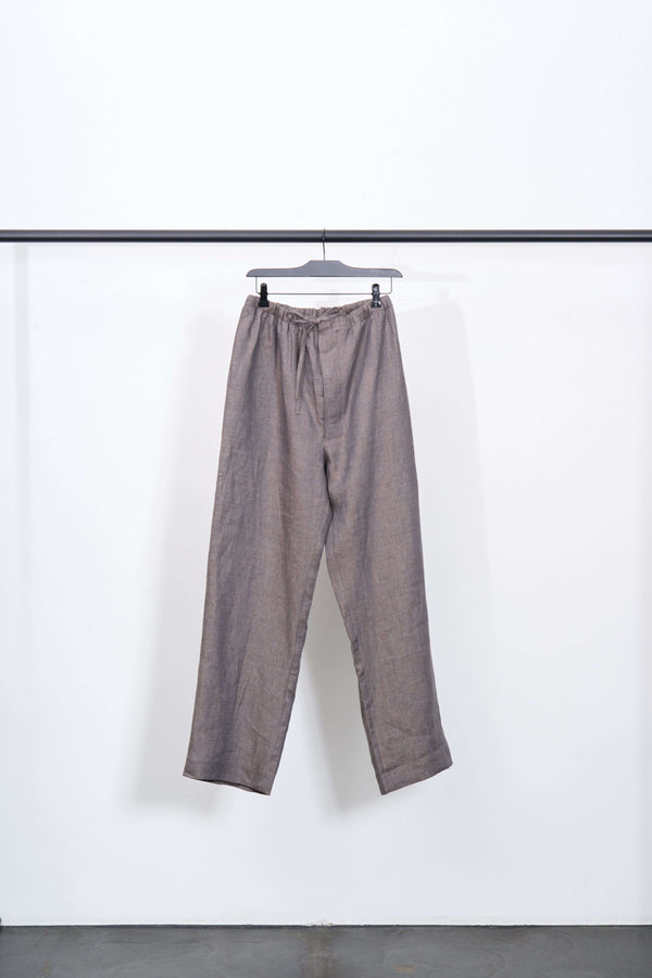 LINEN DRAWSTRING TROUSERS in brown, straight leg style, hanging on a minimalistic rack.