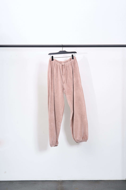PILLOW SWEATPANTS hanging on a black rack against a white background, showcasing a soft pink color.