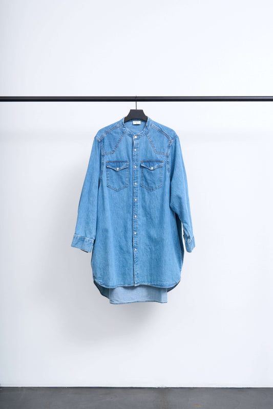 WESTERN DENIM SHIRT DRESS hanging on a black rack against a white wall, showcasing oversized silhouette and snap buttons.