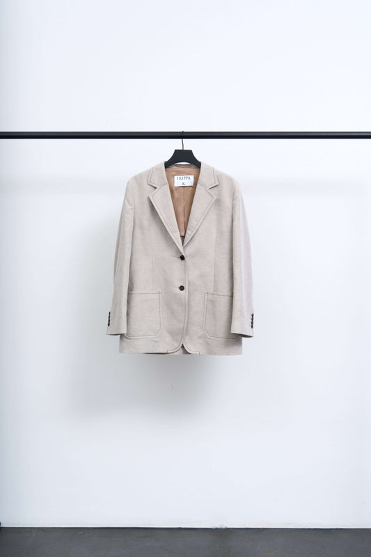BROOKE LINEN MARINER BLAZER hanging on a rack against a white background, showcasing its relaxed tailoring and light texture.
