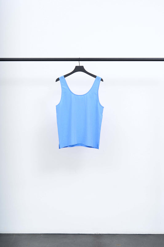 SIKA - LIGHT TENCEL SINGLET hanging on a black hanger against a white background, showcasing its vivid blue color.
