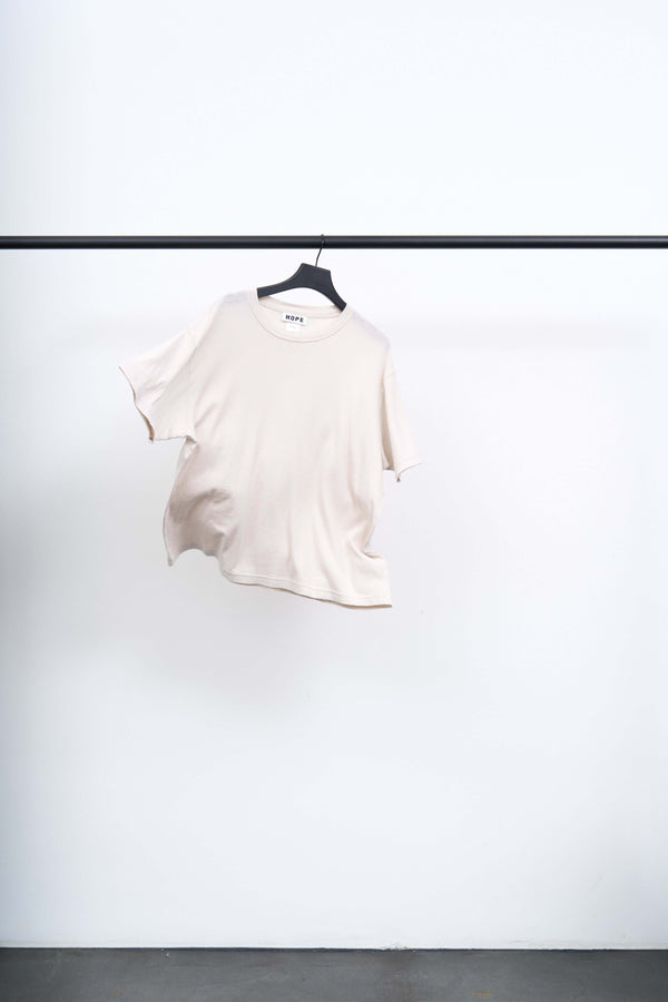 BOXY T SHIRT in soft off-white, featuring a relaxed silhouette, displayed on a hanger against a minimalist backdrop.
