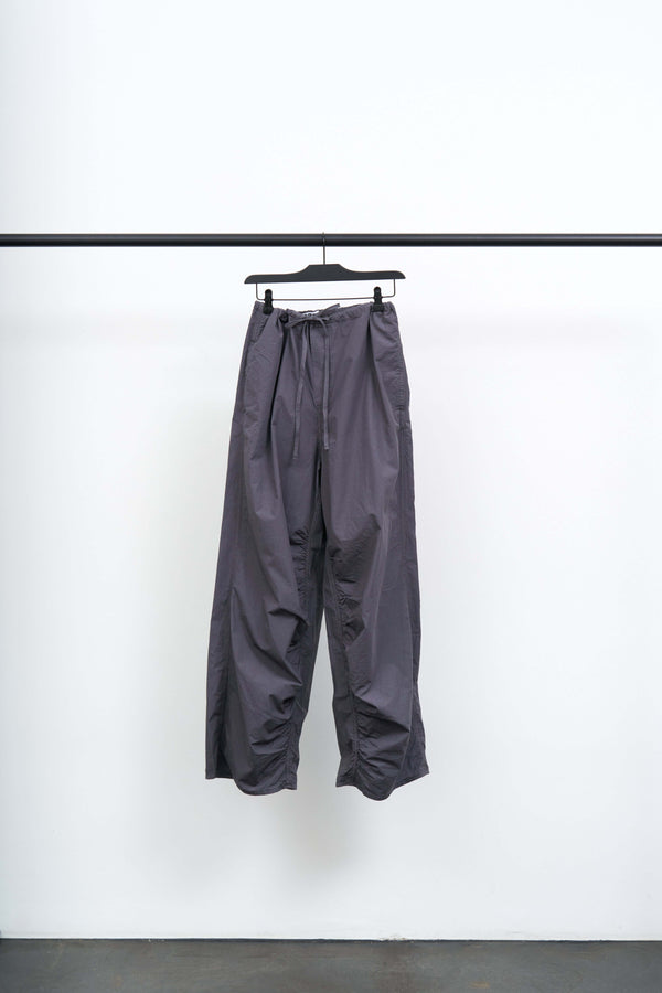 DRAWSTRING TROUSERS in a soft grey hanging on a rack, showcasing their loose fit and lightweight design.