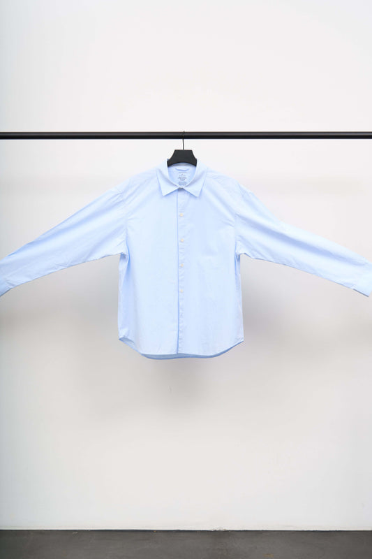 GENEROUS SHIRT displayed on a hanger, showcasing its oversized silhouette in soft light blue organic cotton.