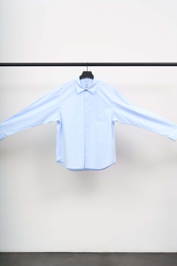 GENEROUS SHIRT displayed on a hanger, showcasing its oversized silhouette in soft light blue organic cotton.