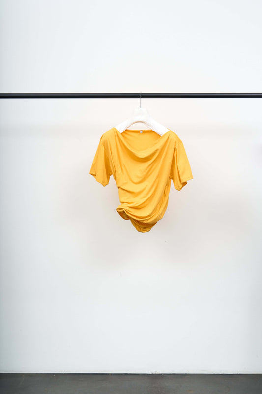 TURN TEE SHIRT in mango yellow hanging on a black rack, showcasing its soft organic cotton fabric.