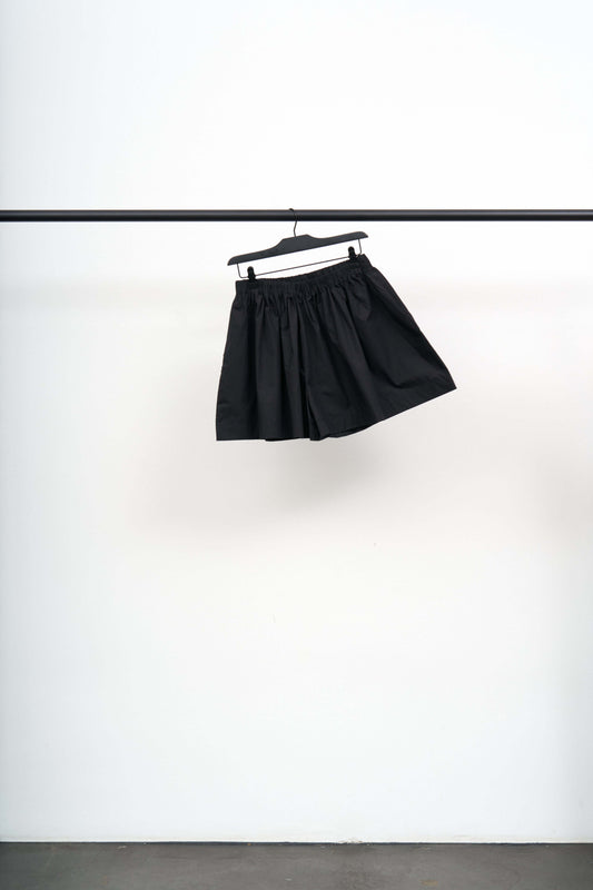 CABLE SHORTS hanging on a rack, showcasing the light black cotton poplin fabric with a unique puff shape.