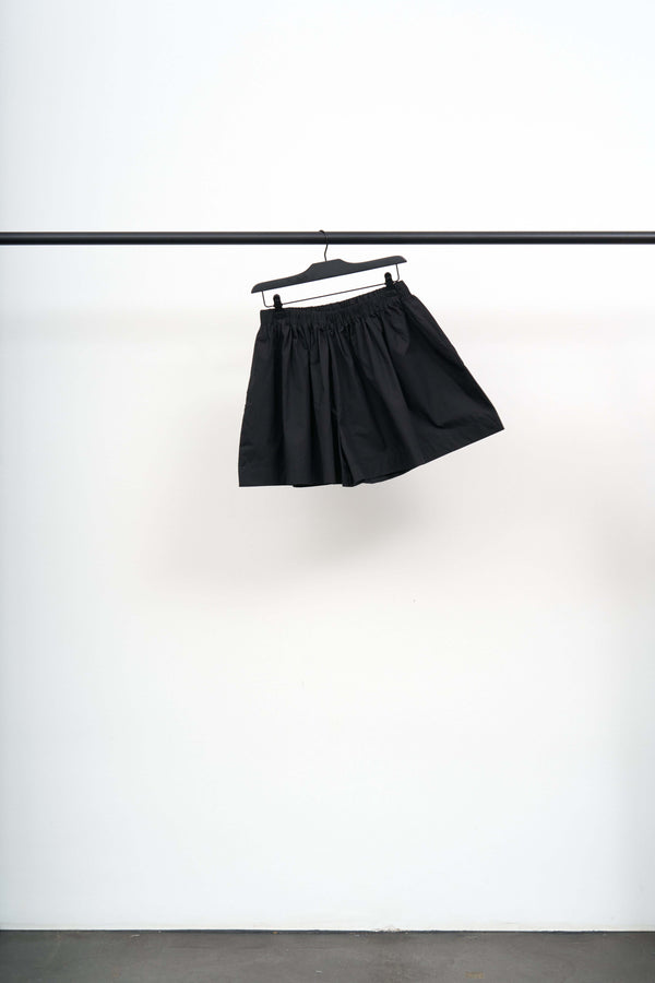 CABLE SHORTS hanging on a rack, showcasing the light black cotton poplin fabric with a unique puff shape.